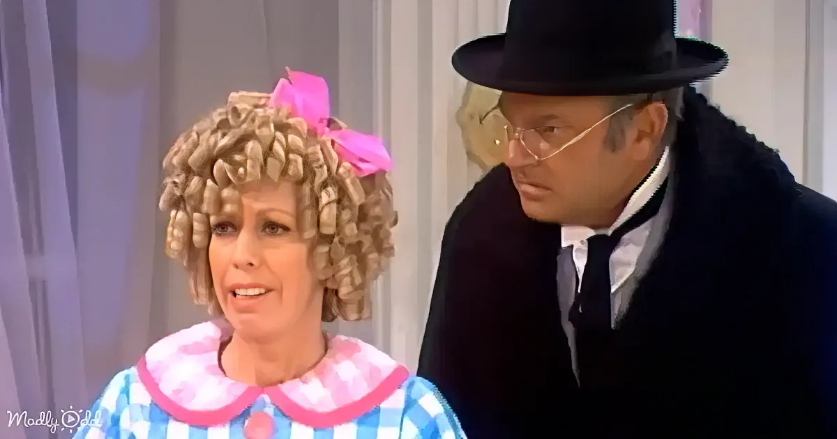 A woman with a curly blonde wig and pink bow, wearing a blue and white checkered dress, stands next to a man in a black...