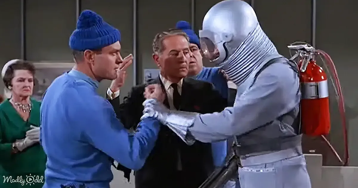 A man in a blue beanie and gloves confronts a silver-suited figure, while others observe in a tense scene.