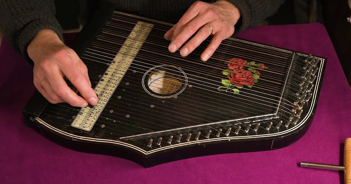 A person plays a zither with a floral design, using their fingers to press the strings.