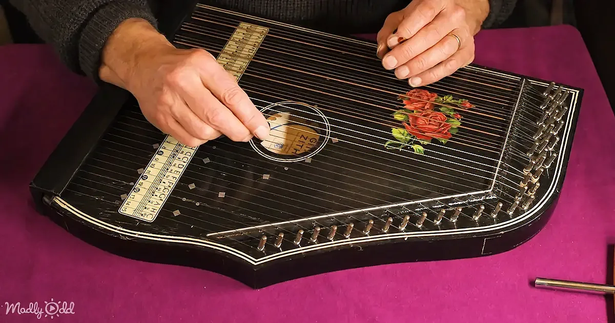 A person plays a zither with a floral design, using their fingers to pluck the strings.