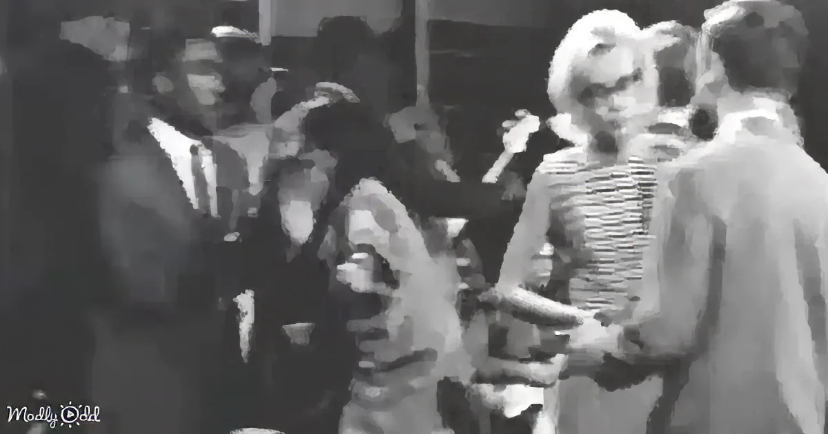 A woman in a striped dress is surrounded by a group of people, possibly at a social event.