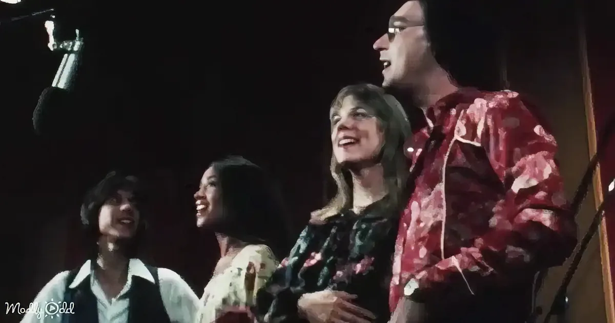 A man in a red patterned shirt stands with three women, all smiling and looking to the left.