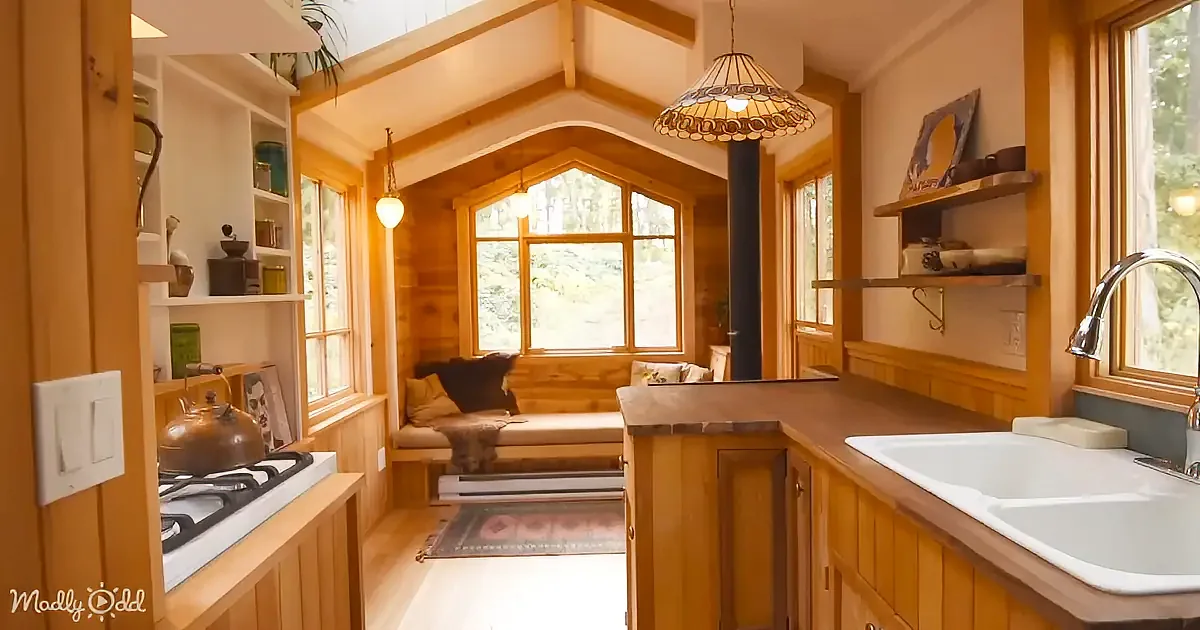 A cozy kitchen with wooden cabinets, a gas stove, a double sink, and a window seat with a view.