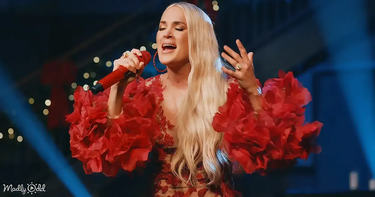 A woman in a red floral dress sings passionately, holding a microphone, with a blurred stage background.