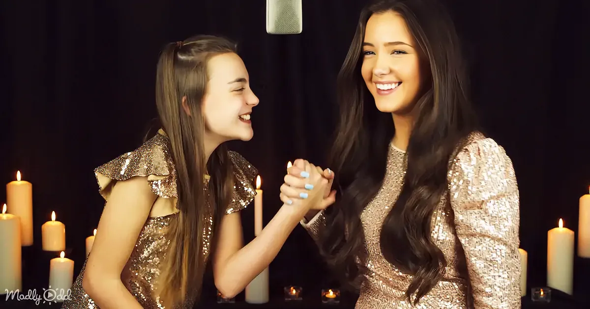 Two women in sparkly dresses hold hands, surrounded by candles, smiling warmly.