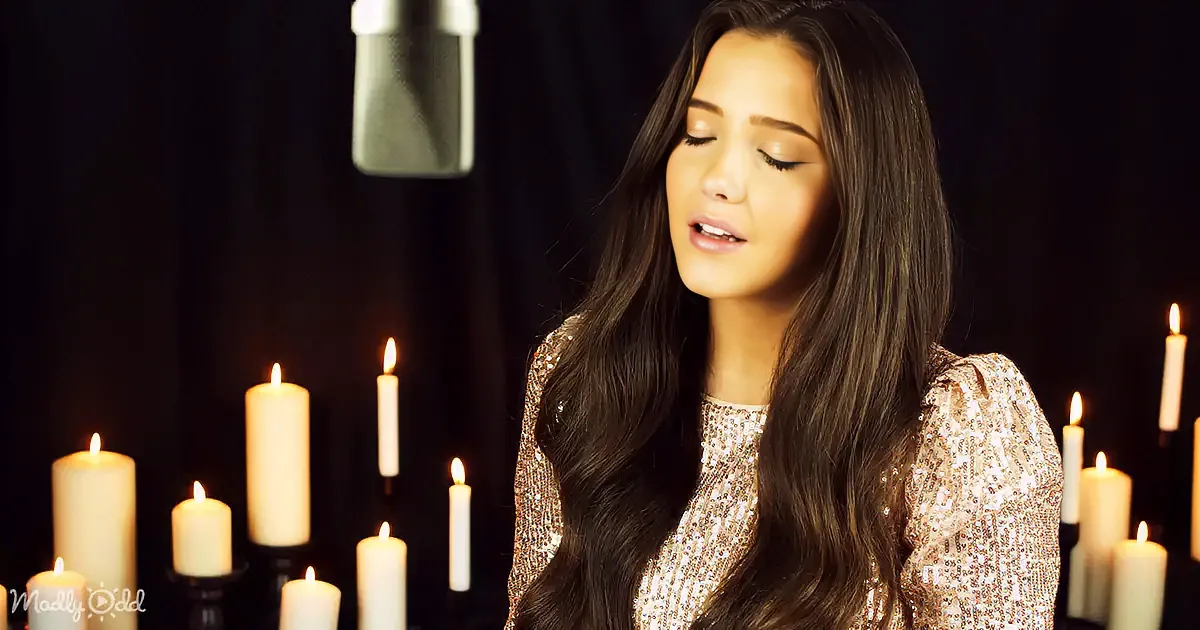 A woman in a sequined top sings with closed eyes, surrounded by lit candles against a dark background.