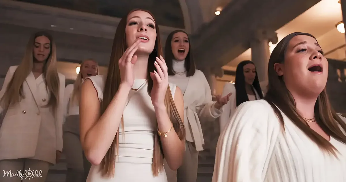A woman in a white dress sings passionately, surrounded by others in a church-like setting.