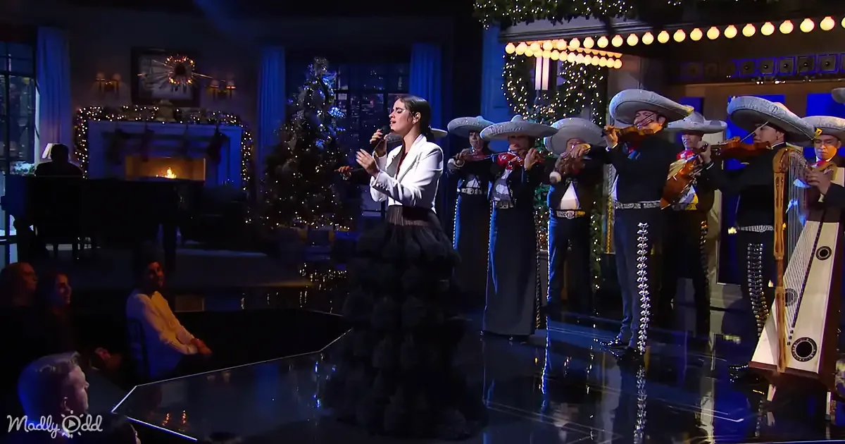 A woman in a black dress sings on stage with a mariachi band, surrounded by festive decorations.