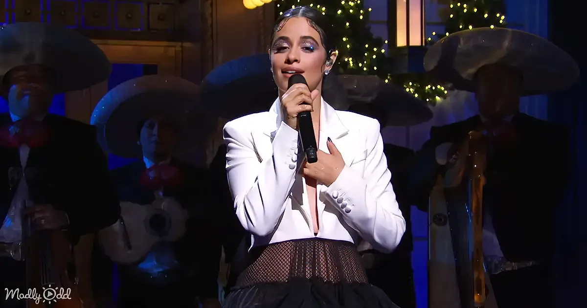 A woman in a white blazer sings into a microphone, surrounded by musicians in sombreros.