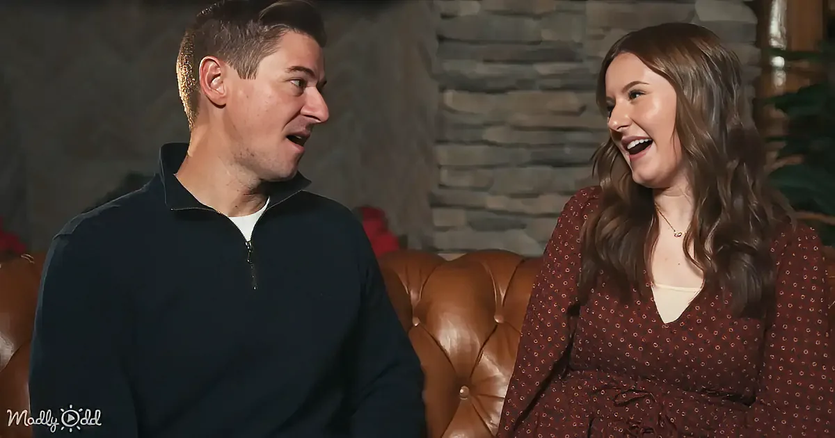 A man and woman are sitting on a leather couch, both smiling and looking at each other.