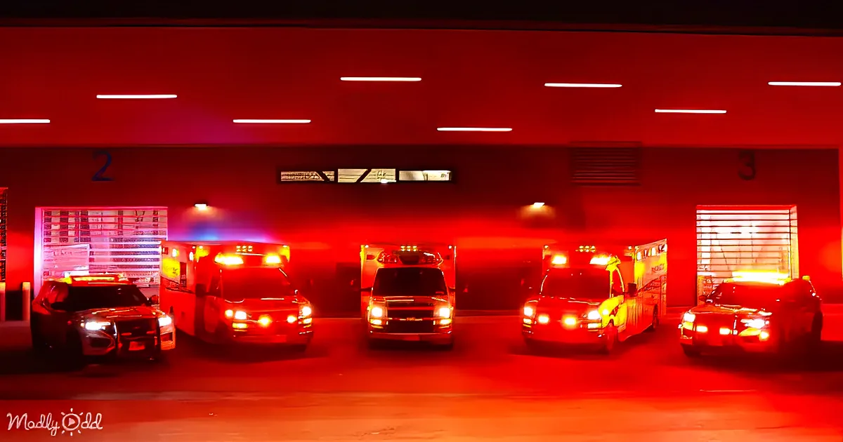 Ambulances and police cars with flashing lights in a garage illuminated by red emergency lights.