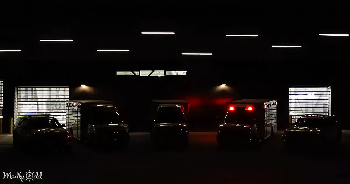 Dark parking lot with several vehicles, including golf carts and police cars, illuminated by red lights.