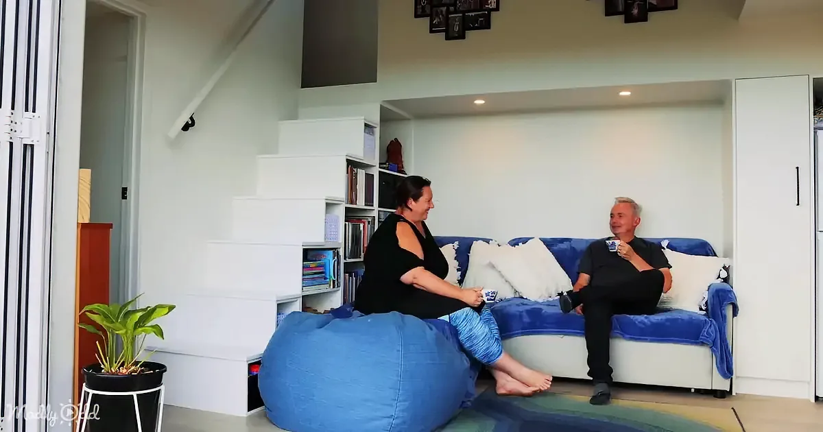 A woman sits on a bean bag, talking to a man on a blue couch in a cozy living room.