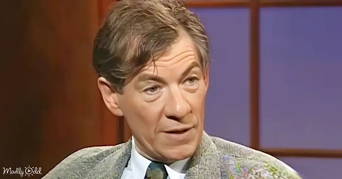 A man in a suit and tie smiles while wearing a textured jacket, set against a backdrop of a window.