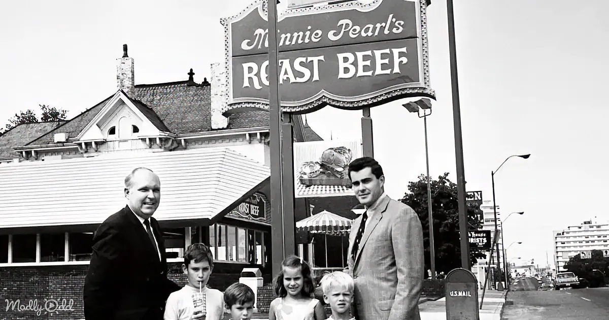 A family stands in front of Minnie Pearl's Roast Beef sign, with a building and street in the background.