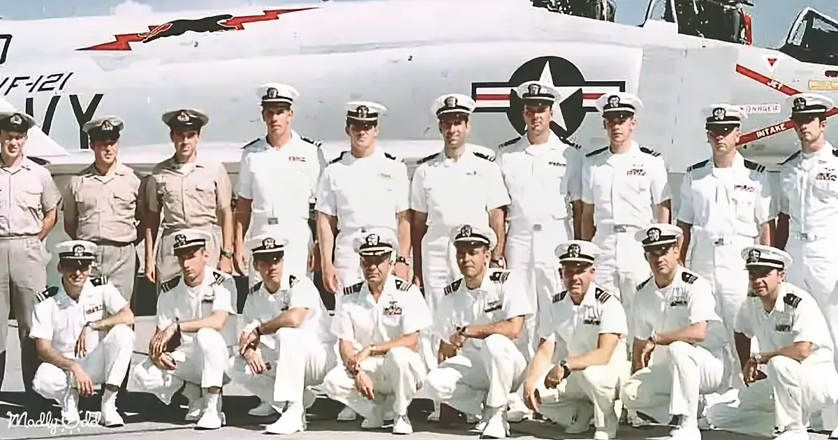 A group of men in white naval uniforms pose in front of a white aircraft with a star emblem.