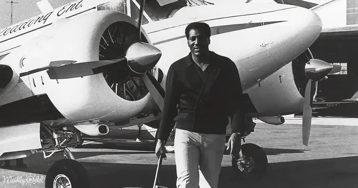 A man walks with luggage in front of a vintage propeller plane.