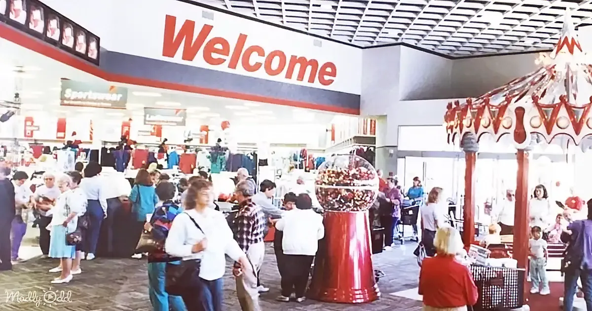 People shop in a bustling department store with a large "Welcome" sign and a red gumball machine.