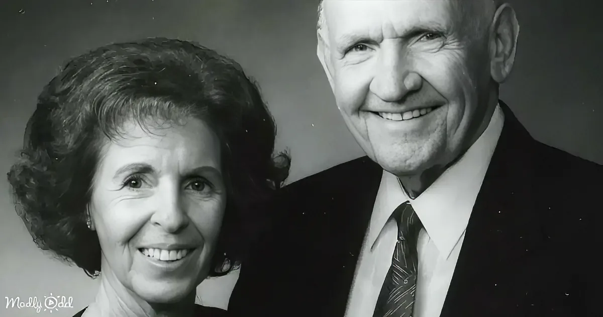 An older couple smiles warmly in a black-and-white portrait, both dressed formally.