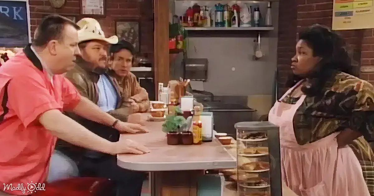 A waitress in a pink apron stands by a table where three men sit, one wearing a cowboy hat.