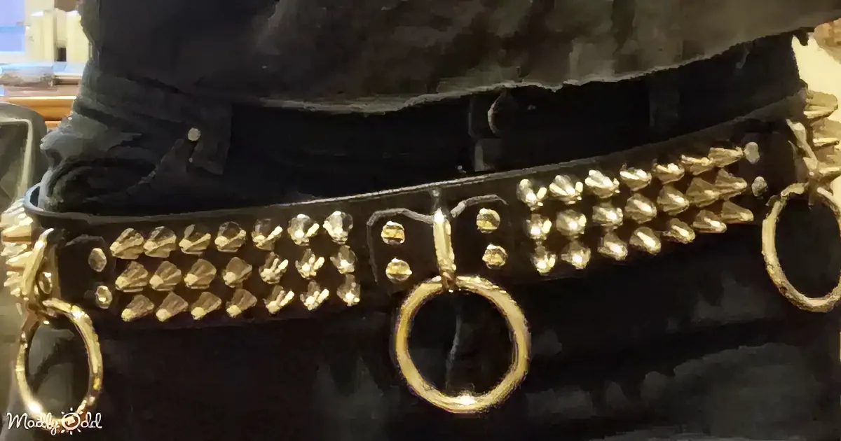 A black belt with gold spikes and rings is worn by a person in dark clothing.