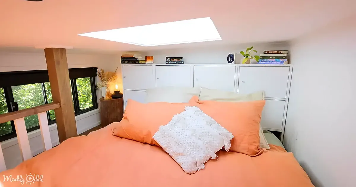 A cozy bedroom with a peach-colored bed, white cabinets, and a skylight above.