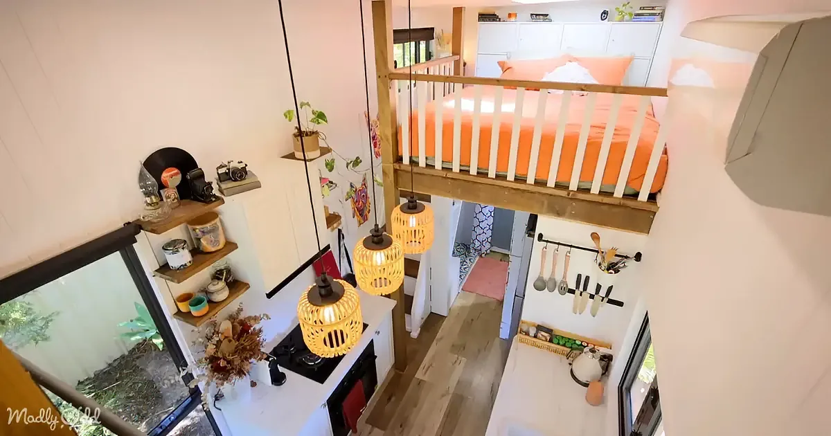 A cozy, compact living space with a loft bed, kitchen, and hanging lights.