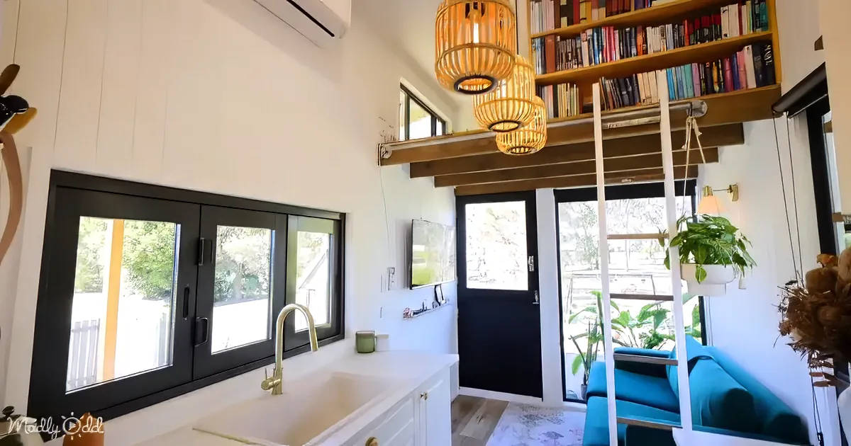 A cozy kitchen with white cabinets, a sink, black-framed windows, and a ladder leading to a bookshelf.