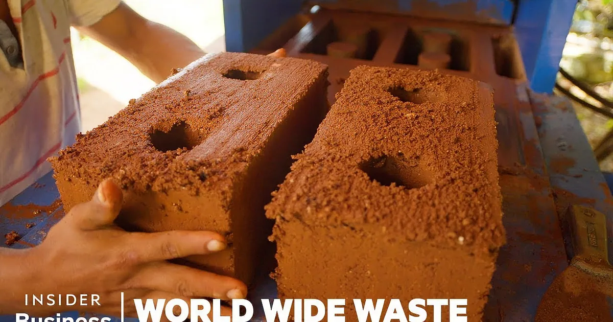 Two hands hold freshly made, textured clay bricks with circular holes on a blue surface.