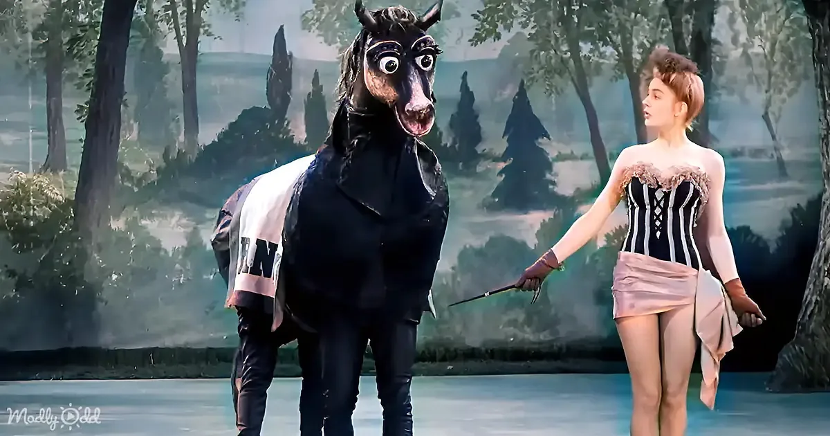 A person in a horse costume and another in a corseted outfit stand on stage with a scenic backdrop.