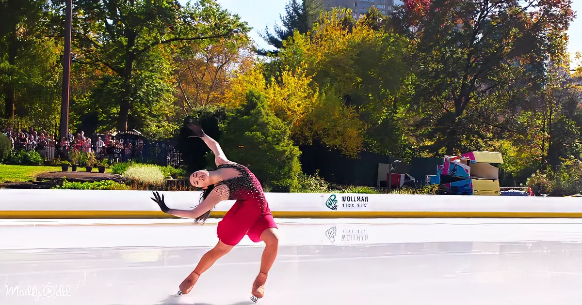 A figure skater in a red dress glides gracefully on ice at Wollman Rink NYC, surrounded by autumn foliage and spectators.