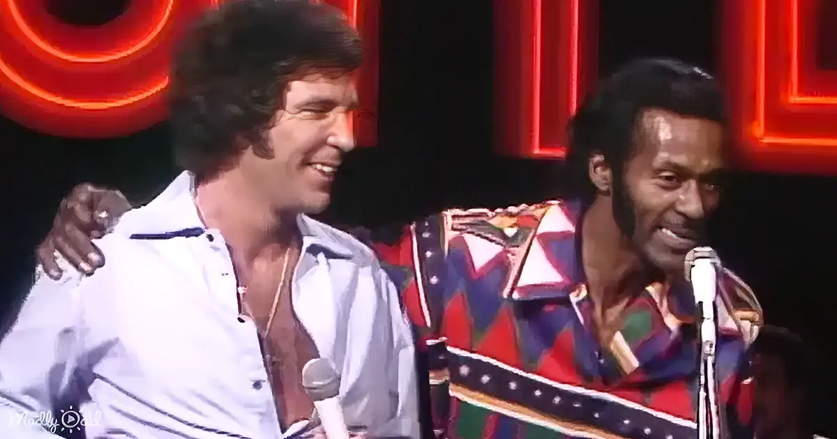 Two men, one in a white shirt, the other in a colorful patterned shirt, are on stage with microphones.