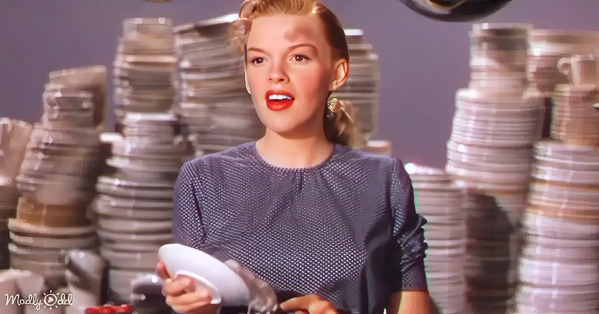 A woman in a grey dress holds a white plate, surrounded by stacks of plates in the background.