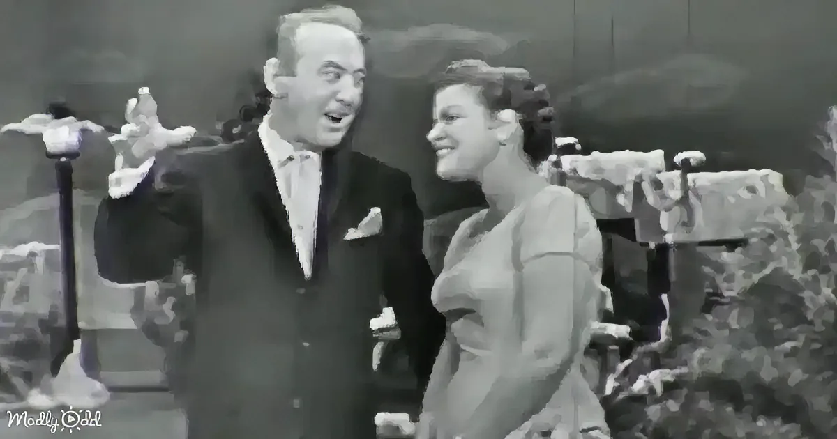 A man in a suit and bow tie gestures animatedly while a woman in a dress smiles beside him.