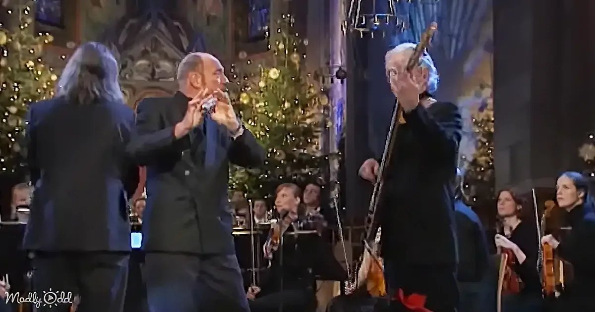 A man in a suit plays a flute on stage, surrounded by musicians and Christmas trees.