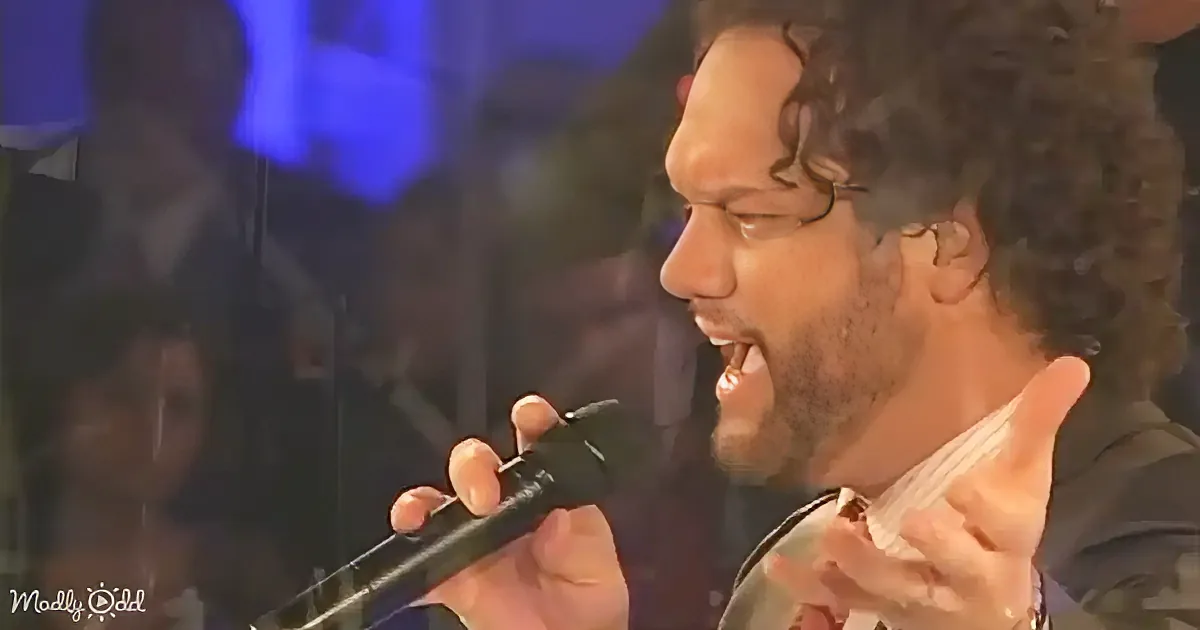 A man with curly hair and a beard is singing passionately into a microphone.