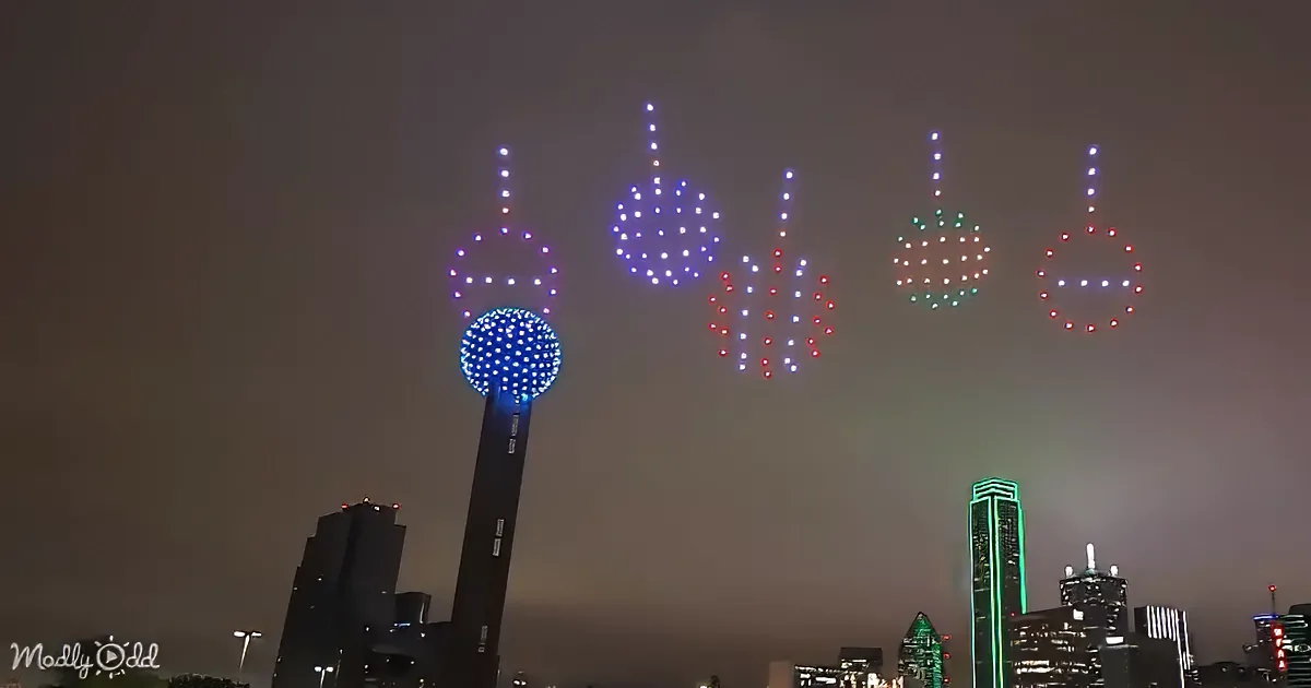 Aerial drone light show forms shapes in the night sky over a cityscape.