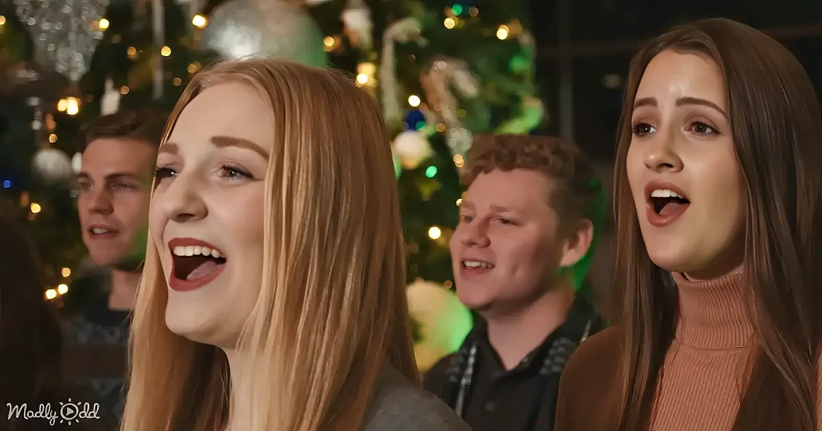 Two women sing in front of a Christmas tree with lights and ornaments.