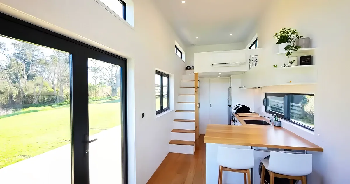 A modern kitchen with a wooden island, white stools, and a staircase leading to a loft.
