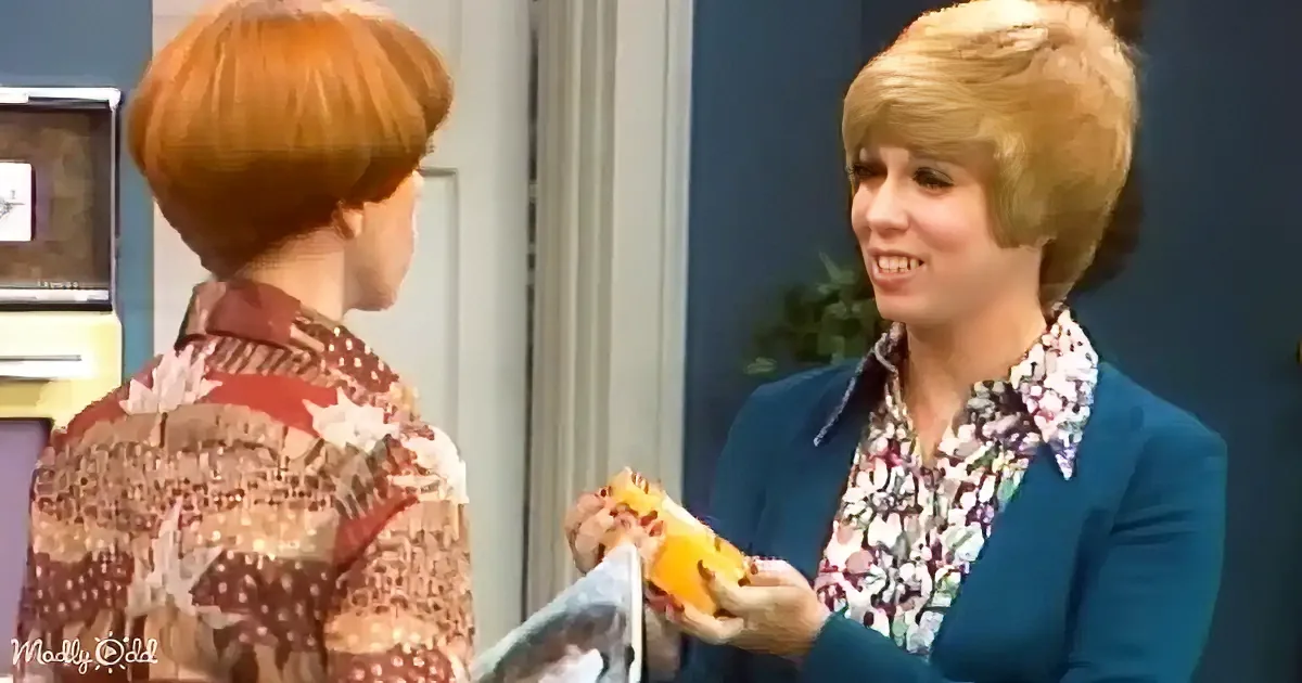 A woman in a floral blouse and blue blazer holds a magazine, smiling at another woman with red hair in a patterned shirt.