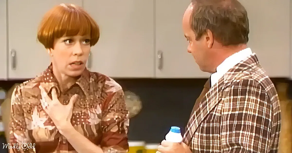 A woman in a floral shirt gestures while talking to a man in a plaid jacket holding a bottle.