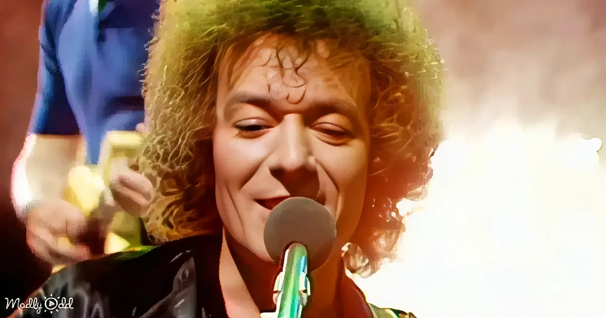 A person with curly hair singing into a microphone, with a bright light source in the background.