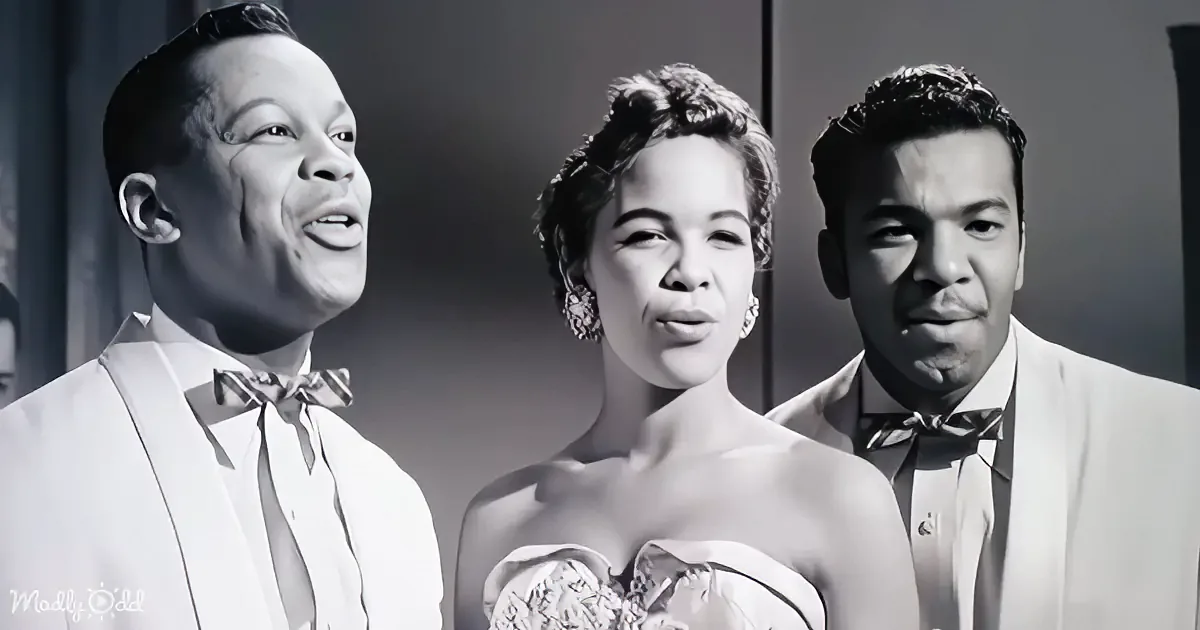 A black-and-white image shows three individuals in formal attire, with one person in the center wearing a strapless dress.