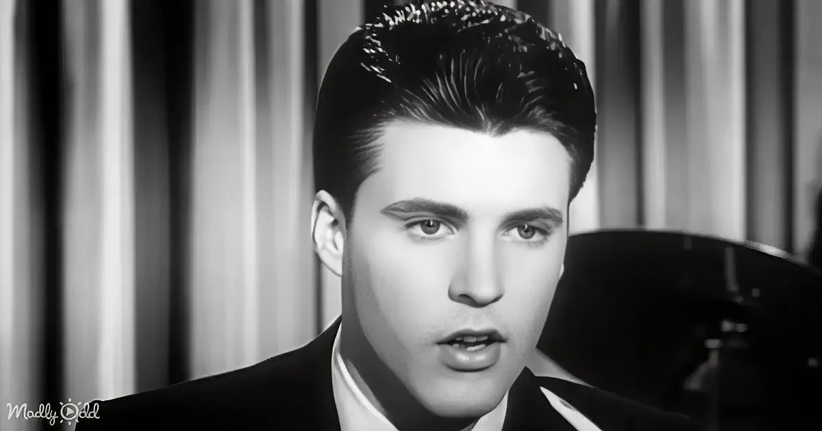 A man in a suit and tie, with slicked-back hair, is looking to the side in a black-and-white image.