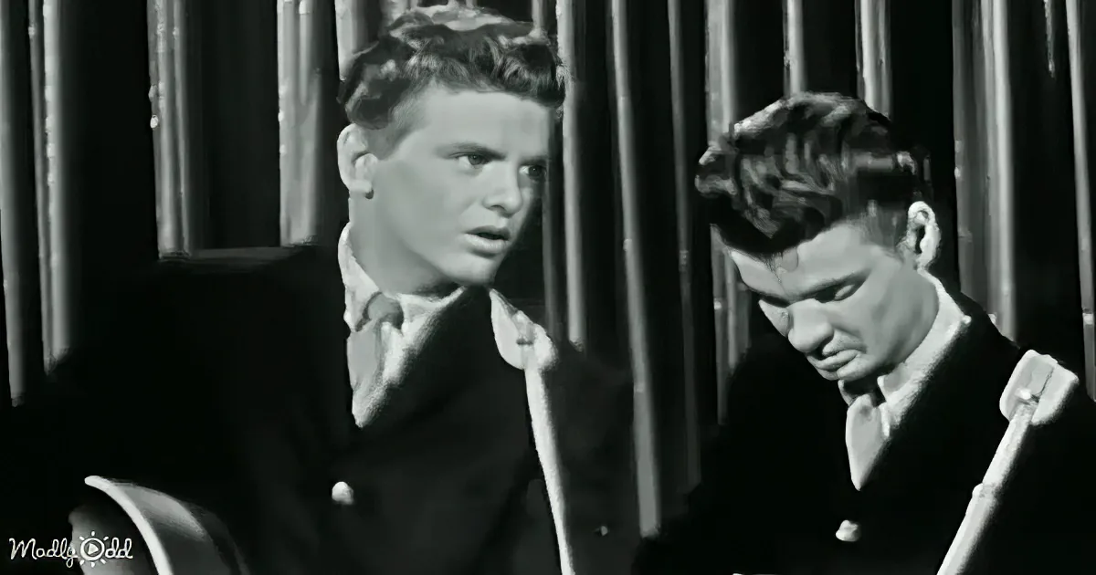 Two men in suits, one looking up, another looking down, in a black-and-white setting.
