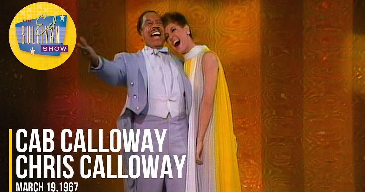 A man in a light blue suit and a woman in a white and yellow dress are smiling and posing together on a stage with a...