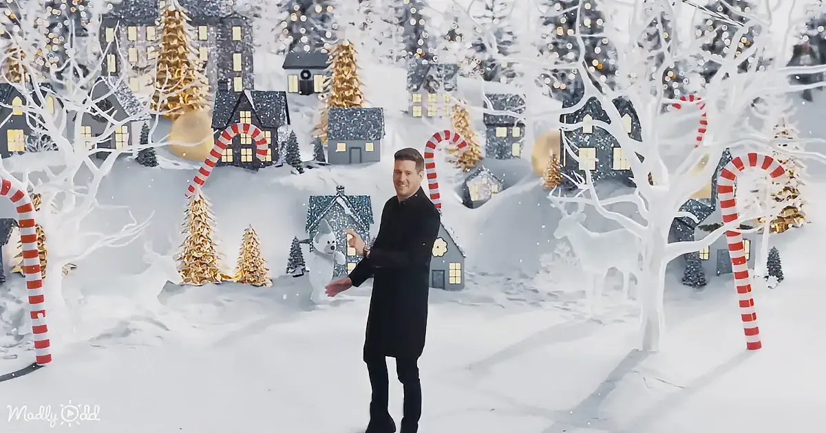 A man in a black coat stands in a snowy, festive village scene with candy canes and illuminated houses.