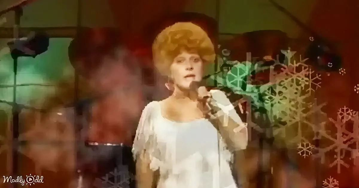 A woman in a white dress sings into a microphone, surrounded by snowflake decorations.