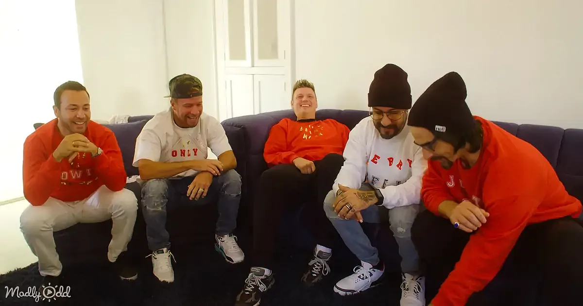 Five men in red and white shirts sit on a couch, laughing and smiling.