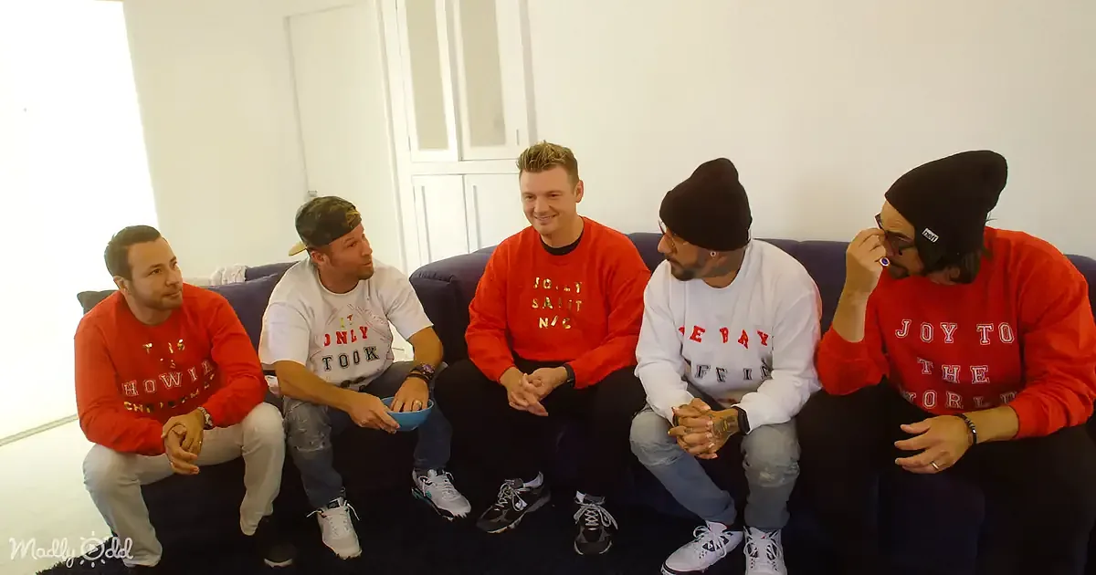 Five men in red and white shirts sit on a couch, engaged in conversation.
